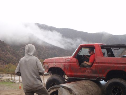 1978 Ford Bronco - A red 1978 Ford Bronco is shown in profile, navigating an off-road obstacle with a driver inside.