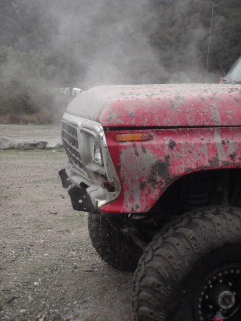 1978 Ford Bronco - This red pickup truck is covered in mud and dust, with smoke or dust billowing from the engine area.