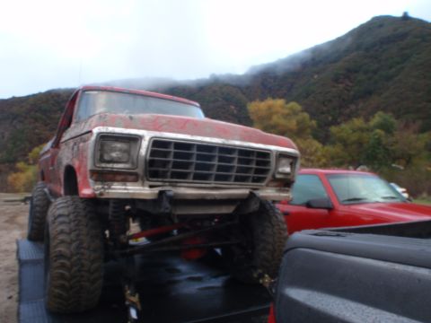 1978 Ford Bronco - A lifted red pickup truck is on a trailer, with another red vehicle visible behind it.