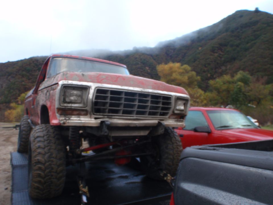 Red pickup truck with large off-road tires on a trailer, front view
