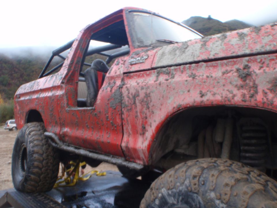 Mud-covered red 1978 Ford Bronco with roll cage, off-road tires, and side steps
