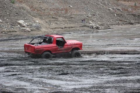 1978 Ford Bronco - A red 1978 Ford Bronco navigates through a muddy terrain, kicking up water and mud.