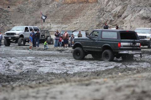 1978 Ford Bronco - A group of off-road vehicles are gathered in a muddy area, with a dark green Ford Bronco in the foreground.