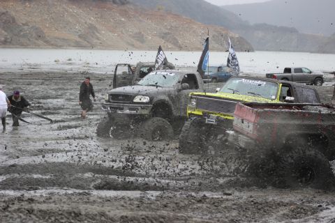 1978 Ford Bronco - Several modified trucks are stuck in thick mud, with people attempting to help them.