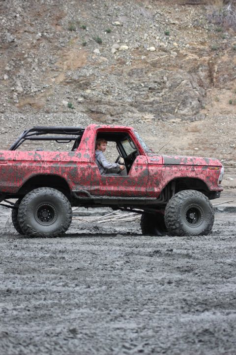 1978 Ford Bronco - A red 1978 Ford Bronco is driven through mud, showing its off-road capabilities.