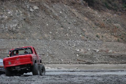 1978 Ford Bronco - A modified red truck with a roll cage is stuck in the mud near a rocky hillside.