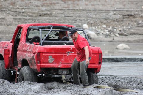 1978 Ford Bronco - A red 1978 Ford Bronco is stuck in thick mud, with a person standing behind it.