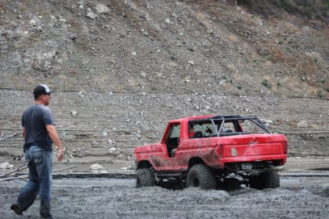 1978 Ford Bronco - A red 1978 Ford Bronco navigates through a muddy terrain, seen from the rear.