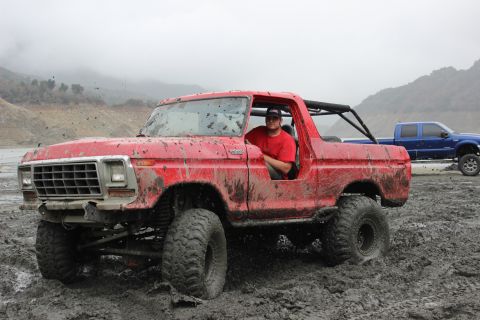 1978 Ford Bronco - A red SUV is stuck in the mud with a man in the driver's seat, while another truck waits behind.