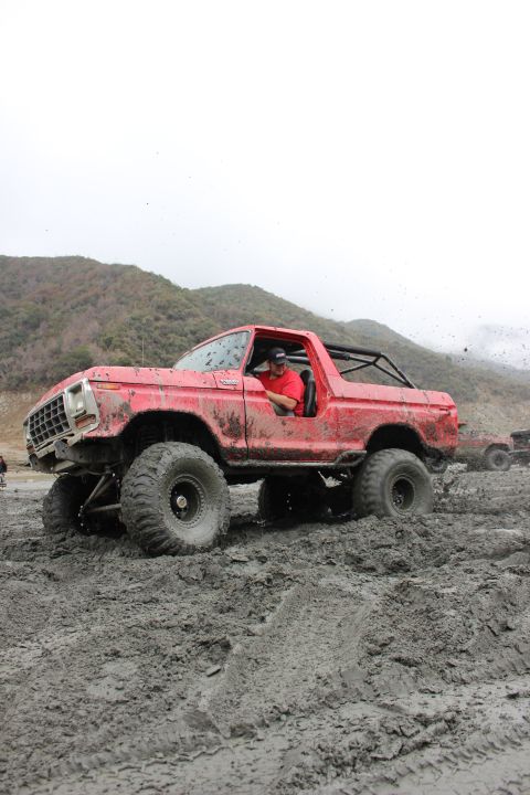 1978 Ford Bronco - A red 1978 Ford Bronco navigates a muddy off-road course, kicking up dirt as it goes.