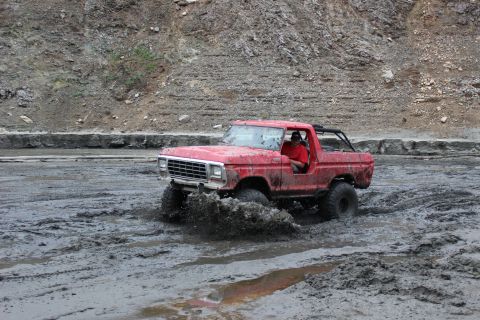 1978 Ford Bronco - Red 1978 Ford Bronco navigates a muddy off-road course, kicking up spray.
