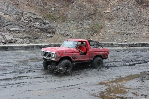 1978 Ford Bronco - A red SUV navigates a muddy terrain with a driver behind the wheel.