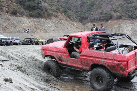 1978 Ford Bronco - A red 1978 Ford Bronco navigates a muddy off-road course with other vehicles in the background.