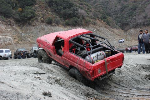 1978 Ford Bronco - A modified red 1978 Ford Bronco tackles a challenging off-road course with other vehicles visible in the background.
