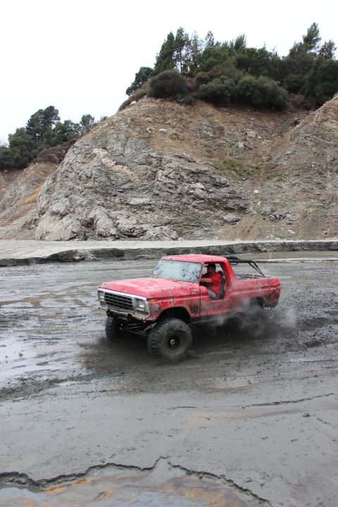 1978 Ford Bronco - This red off-road truck is kicking up mud as it drives through a muddy terrain. The registry claims it is a 1978 Ford Bronco, but the body…