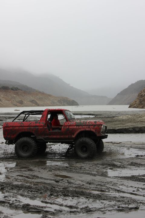 1978 Ford Bronco - Red 1978 Ford Bronco navigating a muddy off-road course with mountains in the background.