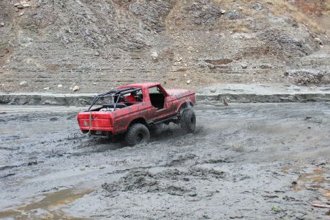 1978 Ford Bronco - A red off-road vehicle navigates a muddy terrain, kicking up spray as it goes.