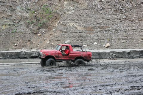 1978 Ford Bronco - A red 1978 Ford Bronco navigates a muddy terrain with a driver at the wheel.
