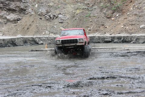 1978 Ford Bronco - A red 1979 Ford F-Series pickup truck navigates a muddy terrain, kicking up water as it drives forward.