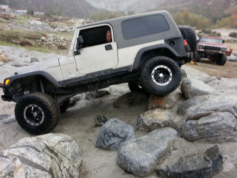 1978 Ford Bronco - A Jeep Wrangler Rubicon is shown off-roading over rocks with another Jeep in the distance.