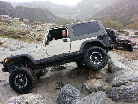 1978 Ford Bronco - A man drives a modified Jeep Wrangler Rubicon over large rocks in a , outdoor setting.