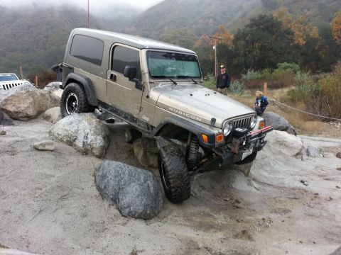 1978 Ford Bronco - Gold Jeep Wrangler Rubicon navigating a rocky obstacle course with another Jeep in the background.