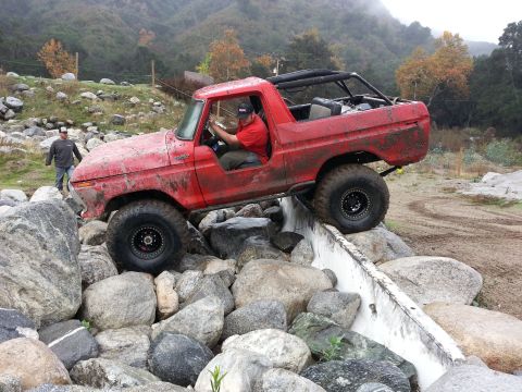 1978 Ford Bronco - A red 1978 Ford Bronco navigates a challenging rocky obstacle on an off-road trail.