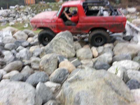 1978 Ford Bronco - A red 1978 Ford Bronco is shown off-roading over a large rock obstacle.