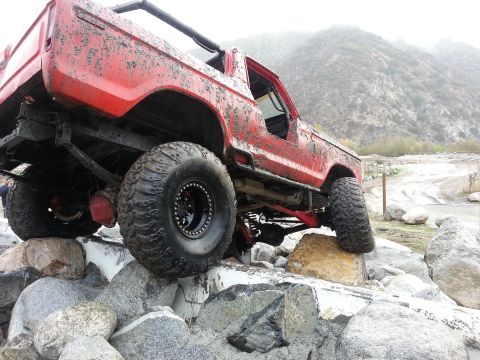 1978 Ford Bronco - This red SUV is navigating a rocky obstacle course, covered in mud.
