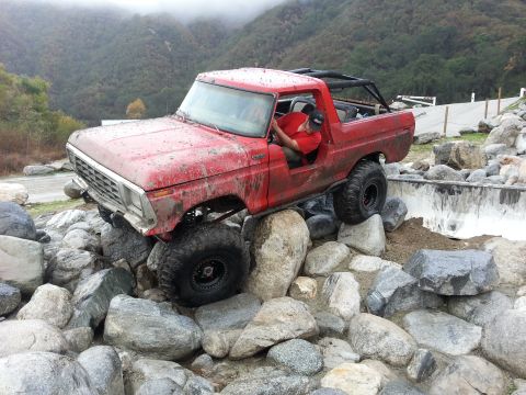 1978 Ford Bronco - Red 1978 Ford Bronco is shown off-roading on a challenging rocky terrain.