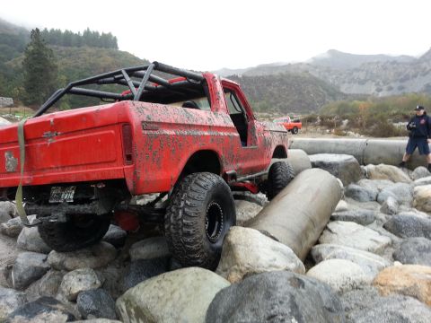 1978 Ford Bronco - A mud-covered 1978 Ford Bronco is driven over large rocks, with another vehicle visible in the background.