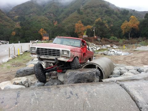 1978 Ford Bronco - A red off-road truck navigates a rocky terrain with large concrete pipes.