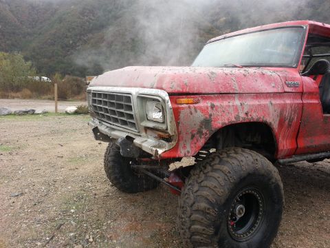 1978 Ford Bronco - Mud-covered 1978 Ford Bronco with smoke billowing from the front, parked on a dirt lot.