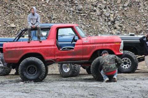 1978 Ford Bronco - A lifted red 1978 Ford Bronco is shown with people around it, possibly during an off-road event.
