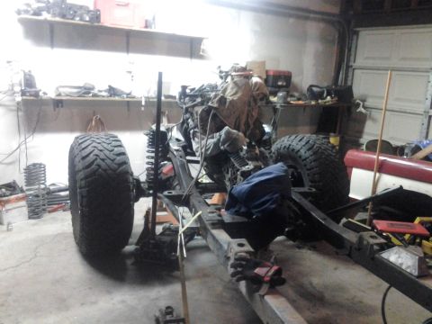 1968 Ford Bronco - Vehicle frame with engine and large tires in a garage, undergoing assembly. Other parts are scattered around.