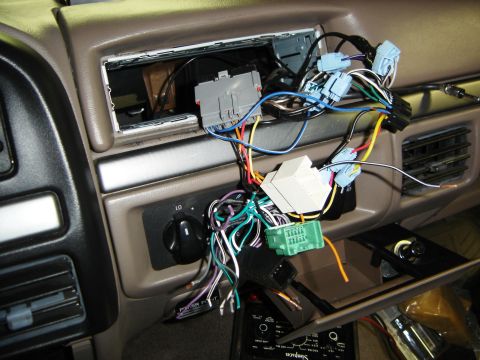 1996 Ford Bronco - Tan interior dash with the radio removed, showing the empty DIN opening and a tangle of wiring harness adapters and multi-colored wires han…