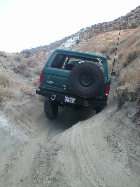 1991 Ford Bronco - 1991 Ford Bronco navigating an off-road trail with a spare tire on the back.