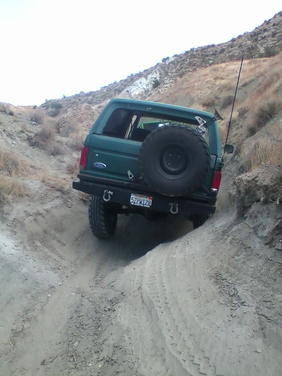 Green 1991 Ford Bronco driving on a dirt trail, spare tire mounted on rear door