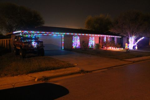 1990 Ford Bronco - A red SUV is decorated with numerous Christmas lights and parked in front of a house adorned with holiday lights.