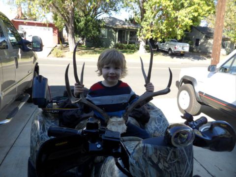 1994 Jeep Cherokee - A young child sits on an ATV with deer antlers, with vehicles parked in the background.