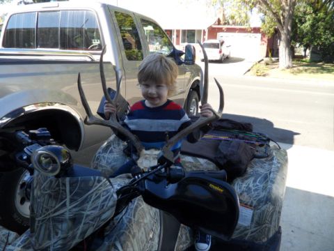 1994 Jeep Cherokee - A young child proudly displays deer antlers while sitting on an ATV, with a pickup truck visible behind them.