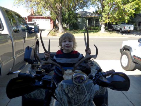 1994 Jeep Cherokee - A child sits on an ATV, holding deer antlers, with vehicles in the background.