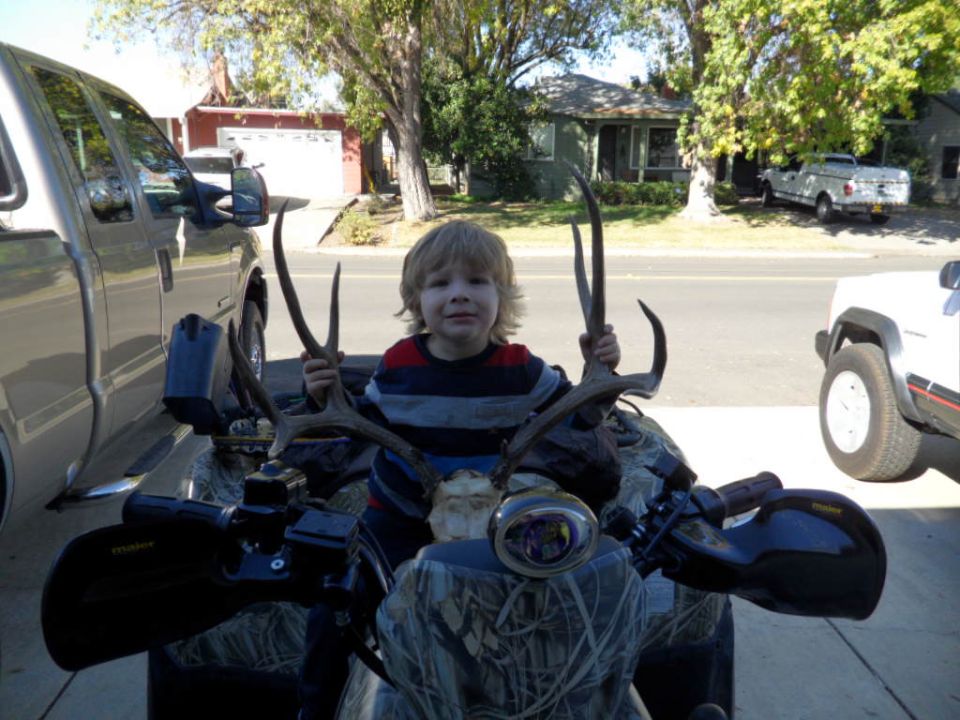 kid on ATV with deer antlers, parked next to a pickup truck and a white Jeep