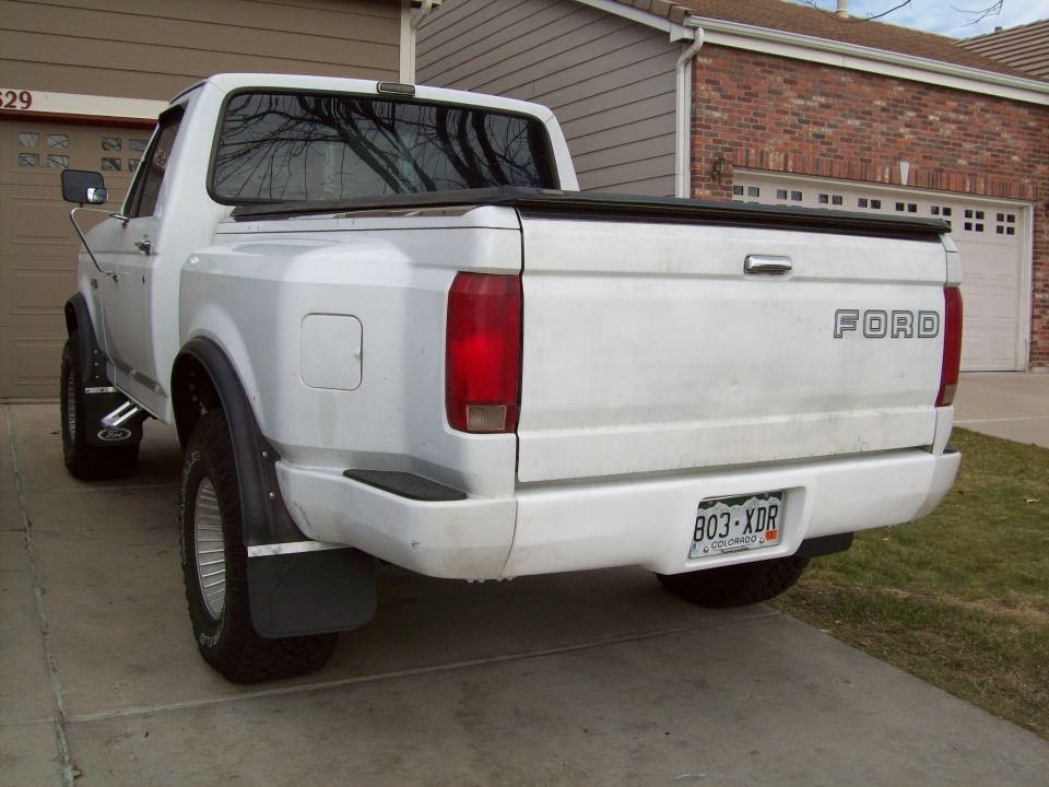 White Ford F-Series pickup truck, rear view, with a tonneau cover and Colorado license plate 803-XDR
