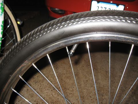 1994 Ford Bronco - A close-up of a bicycle wheel and tire, with a portion of a red car and its license plate in the background.