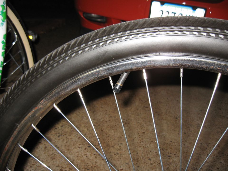Bicycle wheel with a knobby tire and chrome rim, with a red car and license plate visible in the background
