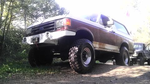 1989 Ford Bronco - This lifted Ford Bronco is parked on a dirt path, with another vehicle visible behind it.