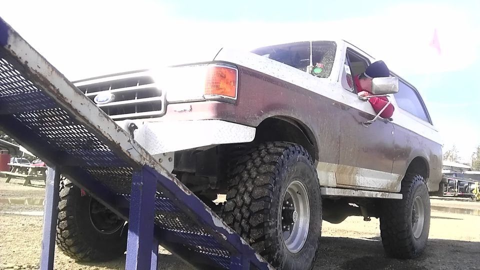 1989 Ford Bronco with large off-road tires on a metal ramp