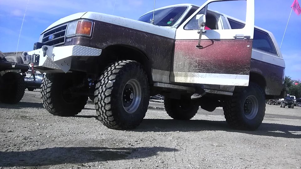 Lifted Ford Bronco with large tires, diamond plate bumper, and open doors