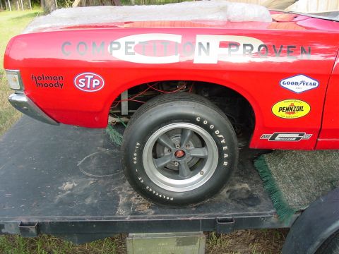 1968 Ford Torino - A close-up view of a red race car's fender displays various sponsor decals, including Holman Moody, STP, Goodyear, and Pennzoil.